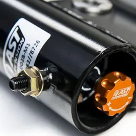 Close-up of a LAST suspension shock absorber featuring an orange adjustment knob, designed for high-performance vehicles. The image highlights the precision engineering and branding details on the black metal casing.