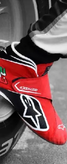 Close-up of a racing suit featuring a red and black design, showcasing a prominent logo and Italian flag colors, highlighting the details of motorsport apparel.