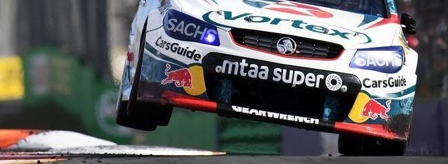 Racing car with Vortex and Red Bull sponsorships airborne during a motorsport event.